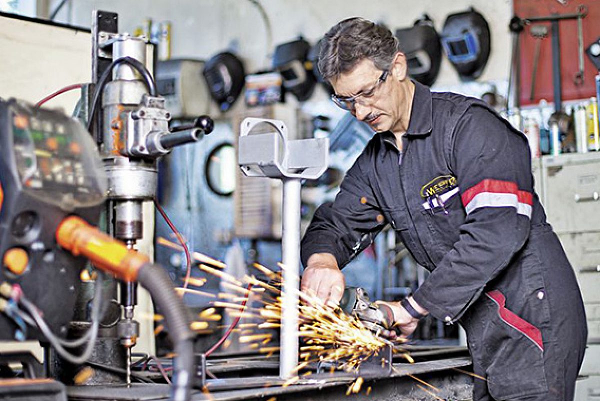 Hans Wepfer in seiner Werkstatt. Im Vordergrund Maschinen, im Hintergrund Hans mit einer Flex am arbeiten